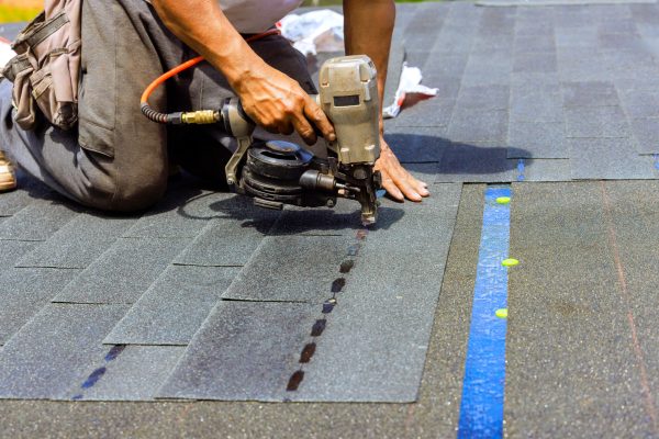 Construction worker used an air pneumatic nail gun when installing new bitumen shingles on roof