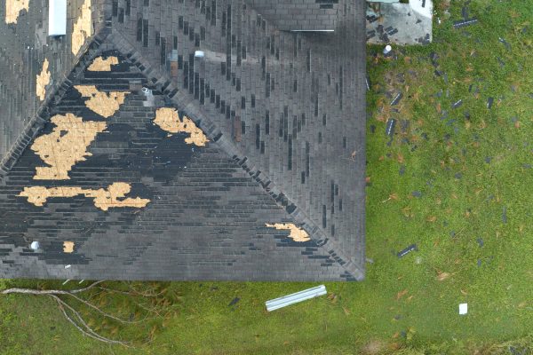 Ruined rooftop in need of repair. Wind damaged house roof with missing asphalt shingles after hurricane Ian in Florida.