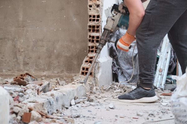 Unrecognizable worker using a jackhammer to drill into wall. Construction site.