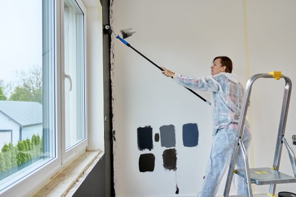 Woman painting white wall in black color using paint roller in modern apartment. Home renovation process, redecoration and interior design updating